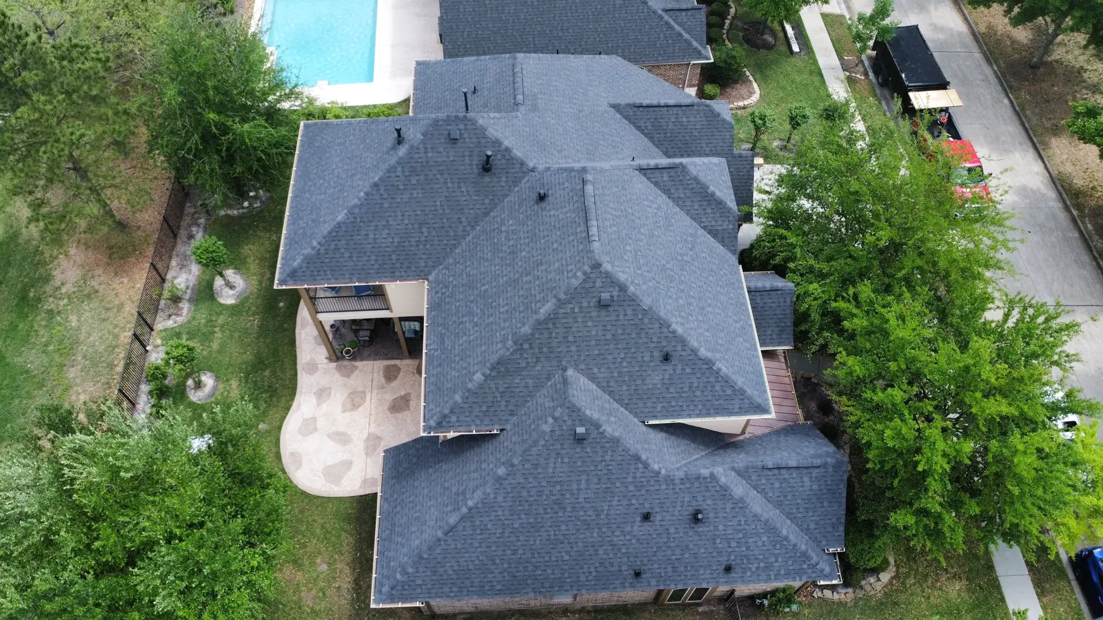 Drone view of a newly replaced charcoal shingle roof above a stamped-concrete patio and pool