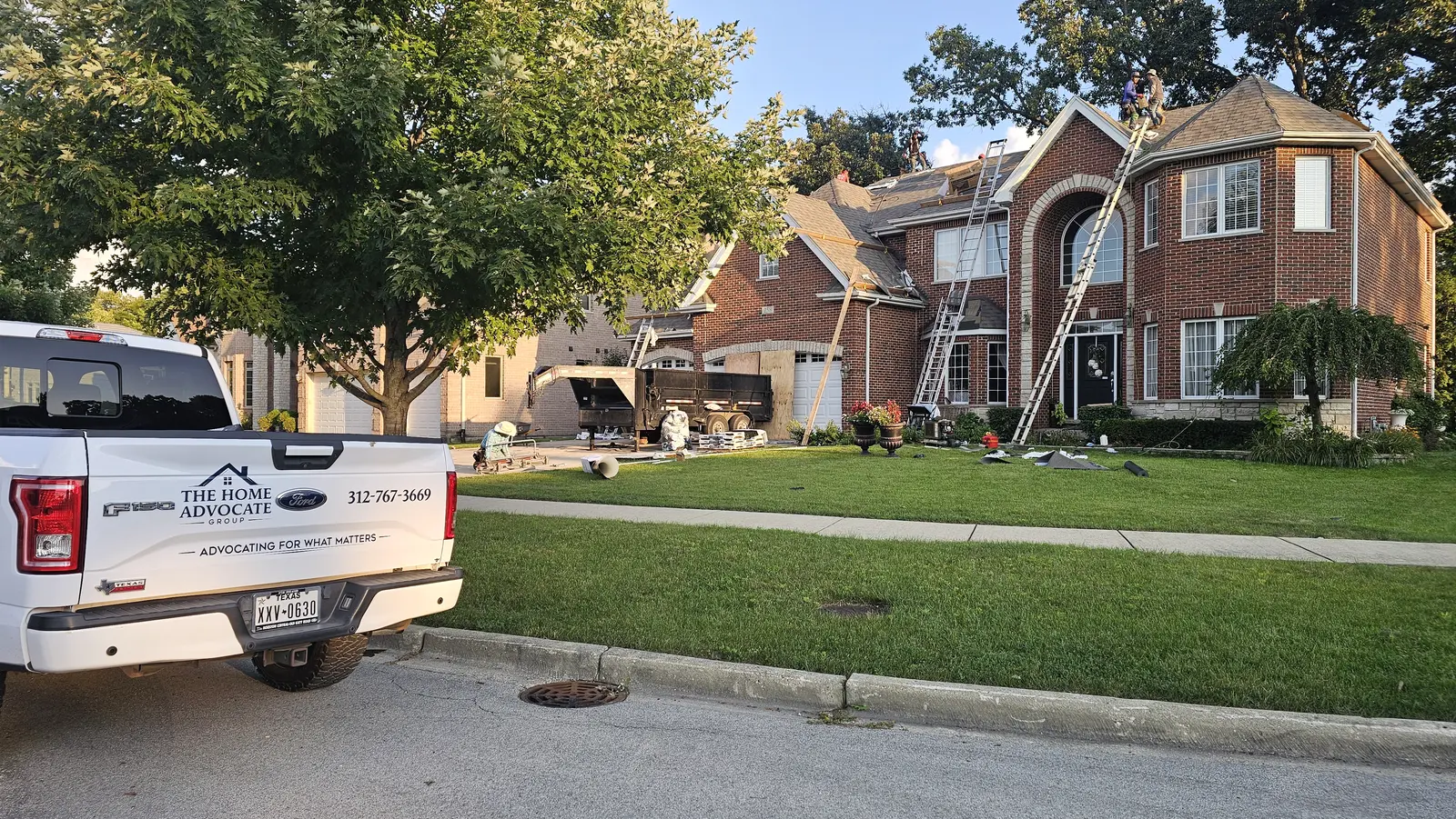 Home Advocate Group truck parked outside a brick home while the crew works on the roof
