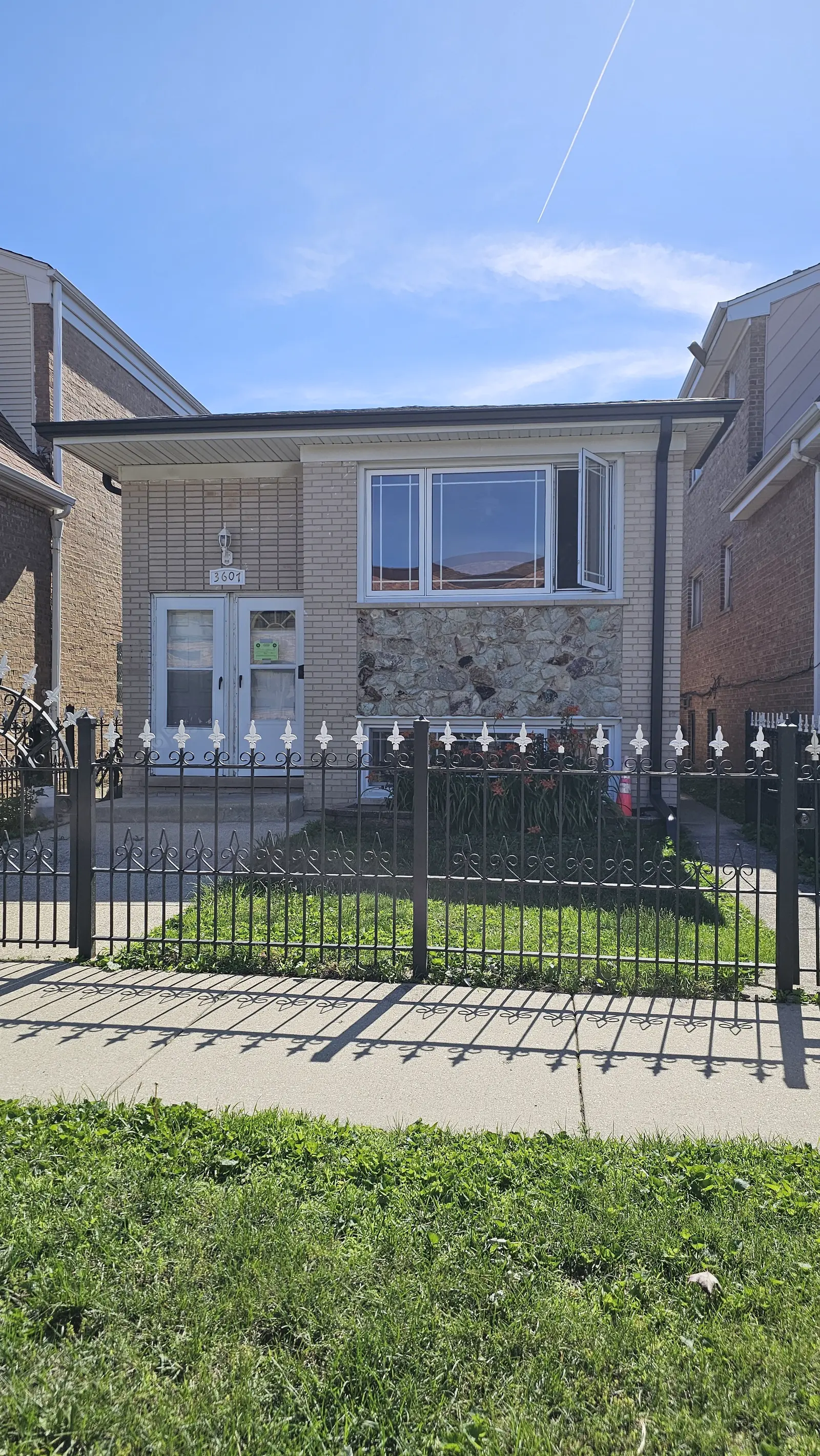 New dark gutters and downspout along the front of a brick home with a wrought iron fence