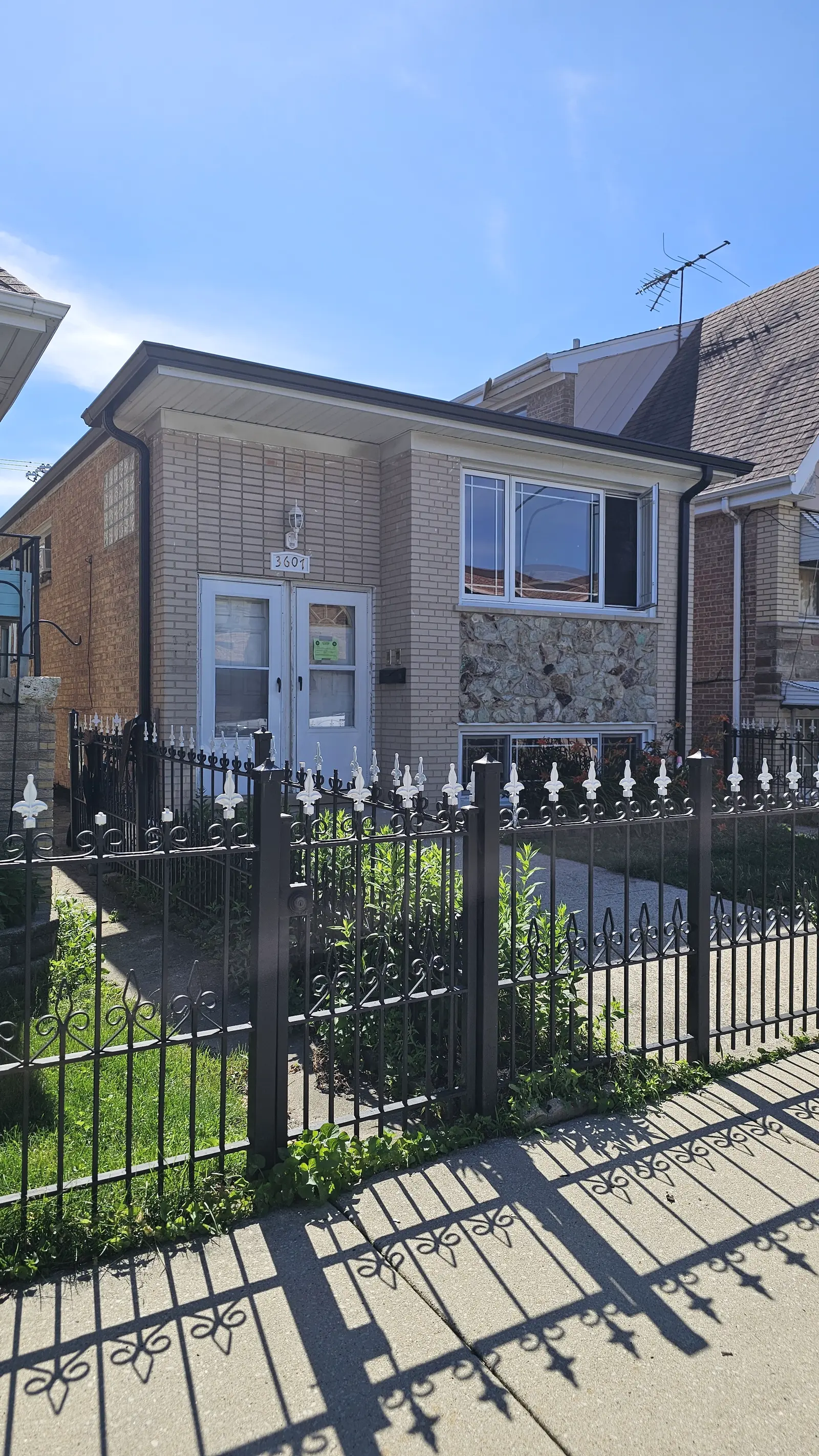 Newly installed dark gutter line and downspout on a brick home seen from the sidewalk